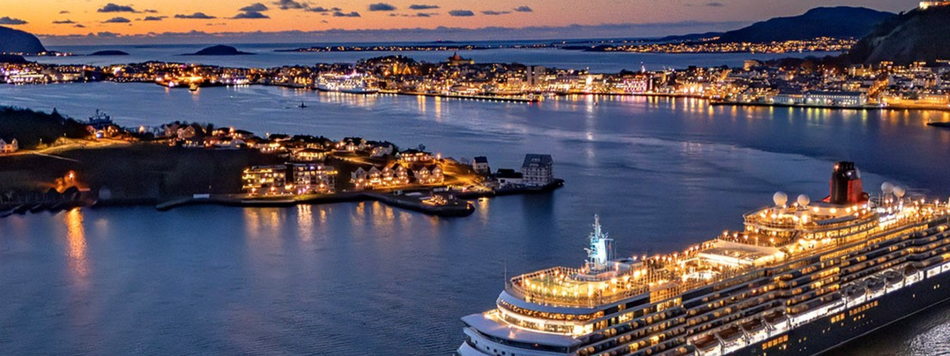 Eit cruiseskip seglar ut frå Ålesund i blåtimen – byen lysar opp i bakgrunnen